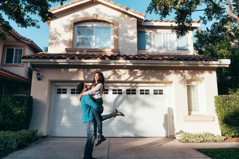 Joyful couple embracing in front of their new suburban house on a sunny day.