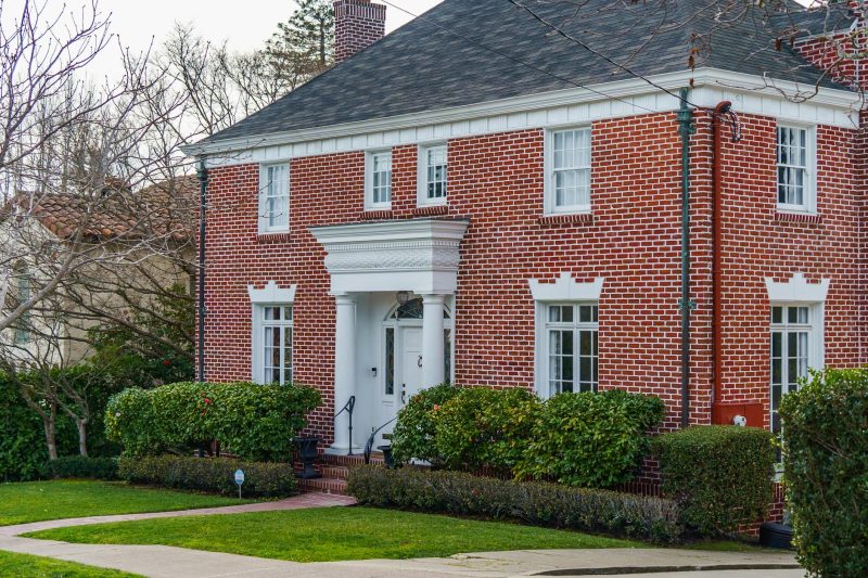 Elegant red brick home surrounded by a lush garden, displaying classic American architectural style.