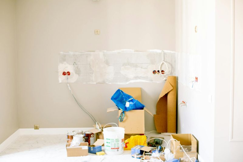 Room in renovation with tools, paint cans, wiring, and supplies scattered on the floor.