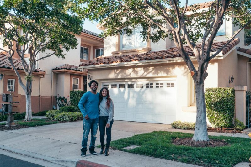 Smiling couple stands proudly in front of their new house, exuding joy and togetherness.