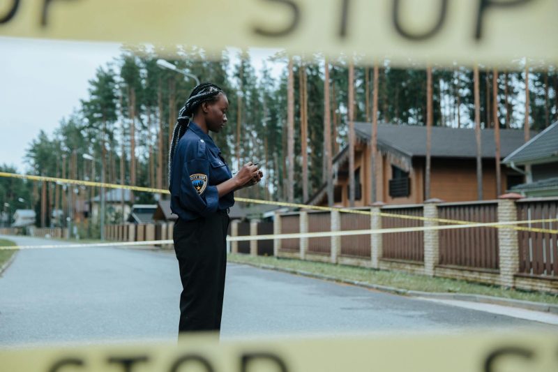 Police officer at a residential street crime scene secured with caution tape.