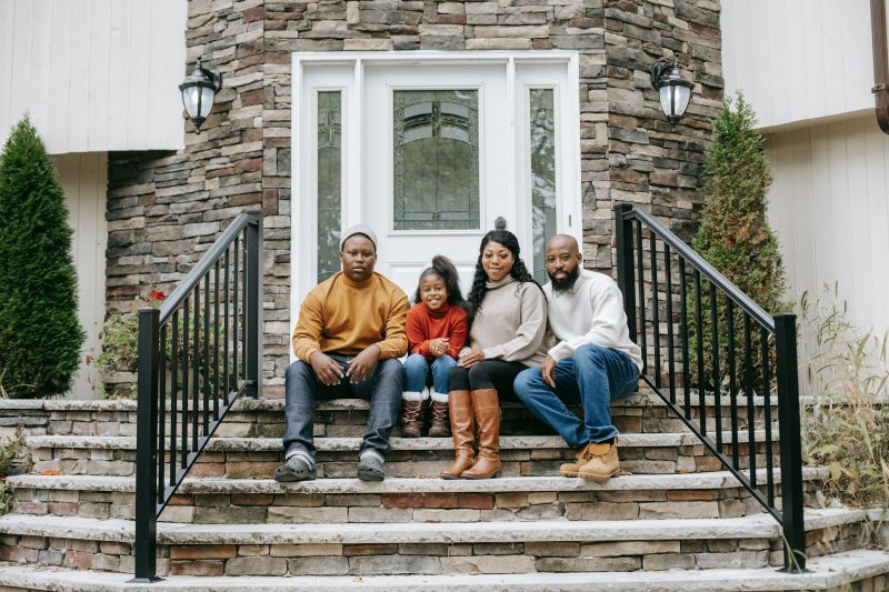 Young African American family, including parents and two children, sitting on a staircase, smiling at the camera.