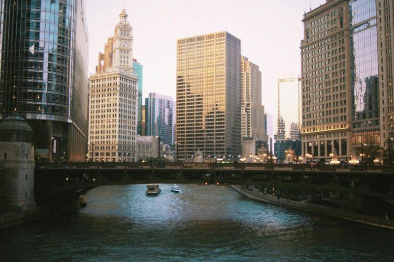 Chicago's river reflects the skyline, featuring historic landmarks and modern skyscrapers against a clear sky.
