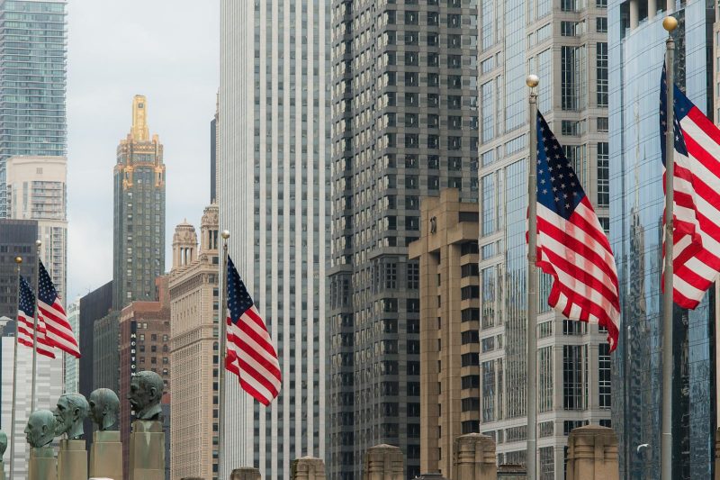 Chicago cityscape with iconic skyscrapers and American flags prominently displayed against a clear sky.
