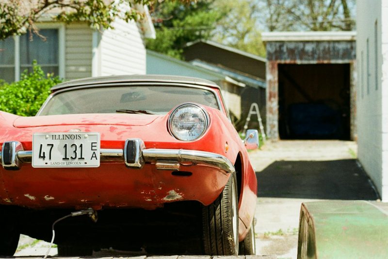 Vintage red car with Illinois license plate parked in a residential driveway surrounded by greenery.