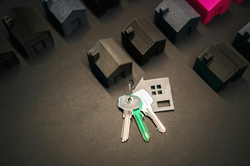 Miniature house models alongside shiny keys on a neutral background.