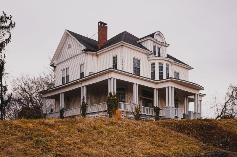 Historic white house with a wraparound porch surrounded by vibrant autumn foliage.