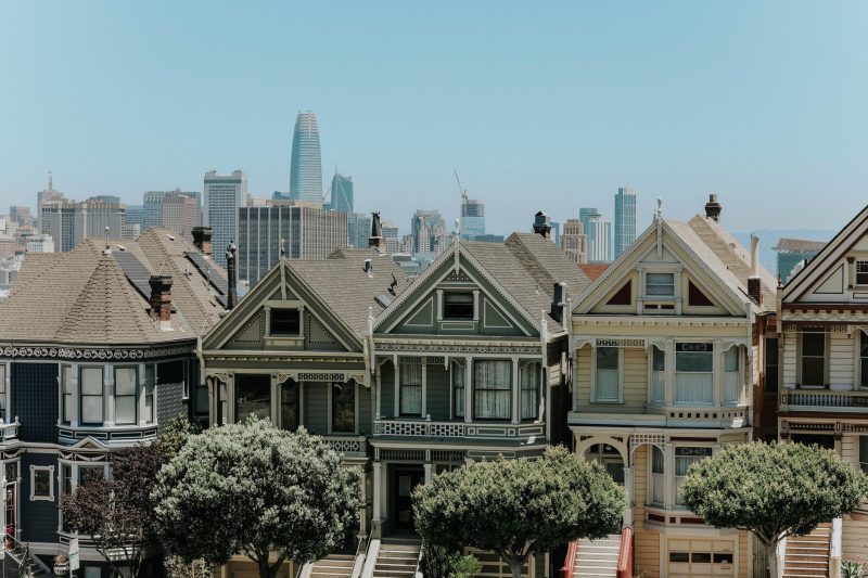 Colorful Victorian houses in San Francisco with a city skyline in the background under a clear blue sky.